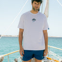 Hombre con camiseta Prisa Cero blanca de Beso Beach sobre un velero en el Mediterráneo